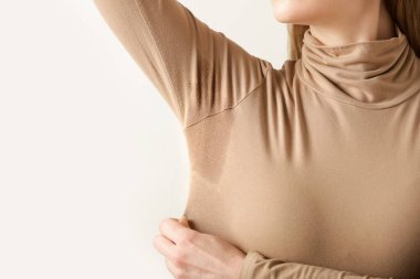 Bej pamuklu balıkçı yaka kazaklı, koltuk altında terli bir kadın resmi.