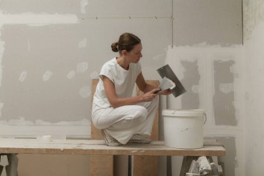 Kadın bantlama ve çamur, alçıpan parçalarını tek bir duvara yapıştırıyor. Alçıpan yüzeyi onarılıyor ve boyama için hazırlanıyor. DIY konut geliştirme projesi.