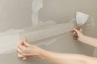 Kadın bantlama ve çamur, alçıpan parçalarını tek bir duvara yapıştırıyor. Alçıpan yüzeyi onarılıyor ve boyama için hazırlanıyor. DIY konut geliştirme projesi.
