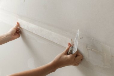 Kadın bantlama ve çamur, alçıpan parçalarını tek bir duvara yapıştırıyor. Alçıpan yüzeyi onarılıyor ve boyama için hazırlanıyor. DIY konut geliştirme projesi.