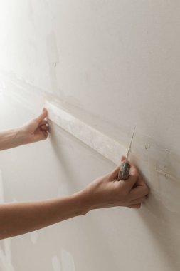 Kadın bantlama ve çamur, alçıpan parçalarını tek bir duvara yapıştırıyor. Alçıpan yüzeyi onarılıyor ve boyama için hazırlanıyor. DIY konut geliştirme projesi.