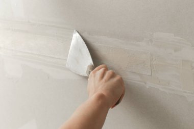 Kadın bantlama ve çamur, alçıpan parçalarını tek bir duvara yapıştırıyor. Alçıpan yüzeyi onarılıyor ve boyama için hazırlanıyor. DIY konut geliştirme projesi.