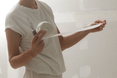 Kadın bantlama ve çamur, alçıpan parçalarını tek bir duvara yapıştırıyor. Alçıpan yüzeyi onarılıyor ve boyama için hazırlanıyor. DIY konut geliştirme projesi.