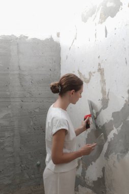 Woman plastering wall with putty-knife. Fixing wall surface and preparation for painting. DIY housing improvement project. clipart