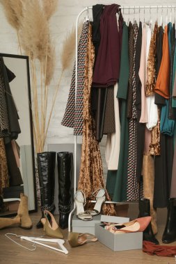 Süslü giysileri ve aksesuarları olan dağınık kadın kıyafetleri. Elbise askısına atılmış dağınık giysiler, yerde. Tüketim, alışveriş ve kompülsif satın alma bozukluğu kavramı.