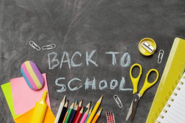 Siyah karatahta arka planında çeşitli ofis ve okul malzemeleriyle okul konseptine geri dönelim..