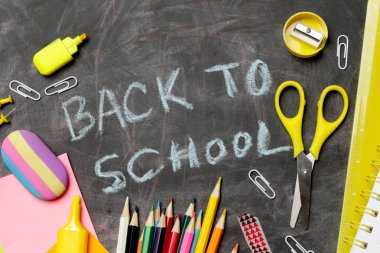 Siyah karatahta arka planında çeşitli ofis ve okul malzemeleriyle okul konseptine geri dönelim..