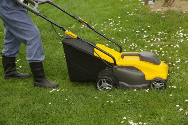 Siyah lastik çizmeli bahçıvan çimleri biçme makinesiyle buduyor.