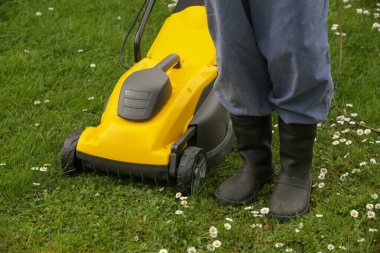 Siyah lastik çizmeli bahçıvan çimleri biçme makinesiyle buduyor.