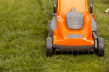 Bahçedeki yeşil çimlerin üzerinde turuncu çim biçme makinesi