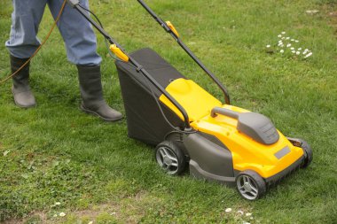 Siyah lastik çizmeli bahçıvan çimleri biçme makinesiyle buduyor.