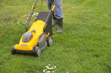 Siyah lastik çizmeli bahçıvan çimleri biçme makinesiyle buduyor.