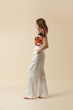 İpek elbise giyen kadın model, mermer turuncu kaşkorse ve beyaz pantolon. Klasik ve basit moda. Stüdyo çekimi.