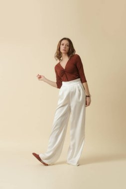 Kahverengi pamuklu ve beyaz pantolon giyen bir kadın model. Klasik ve basit moda. Stüdyo çekimi.