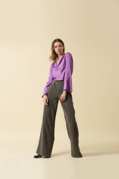 Женщина-модель в фиолетовой шелковой блузке и серых брюках. Классическая и вечная простая мода. Снимок студии.