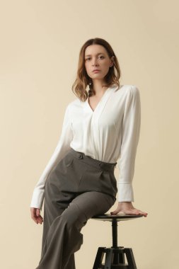 Beyaz bluz ve gri pantolon giyen bir kadın manken. Klasik iş, basit moda. Stüdyo çekimi.