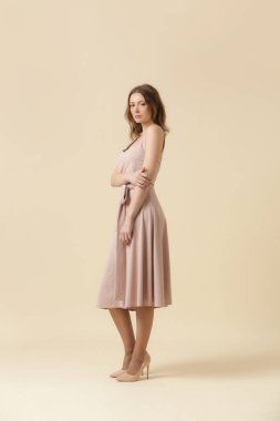  Tek renkli pembe elbise giyen bir kadın manken. Klasik kolsuz bluz ve geniş midi etek. Moda stüdyosu çekimi.