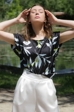 Yazlık bluzlu ve geniş beyaz pantolonlu bir kadın kırsalda huzurlu bir yaz gününün tadını çıkarıyor.