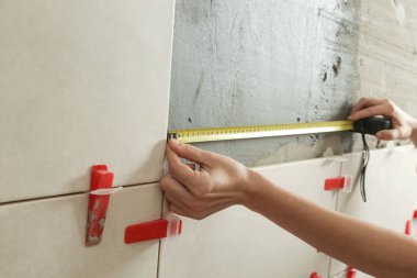 Banyo duvarlarını döşeyen bir kadın, uzunluğu ölçmek için mezura kullanıyor. Banyoya fayans döşeme işlemi adım adım yapılıyor. DIY Ev Geliştirme.