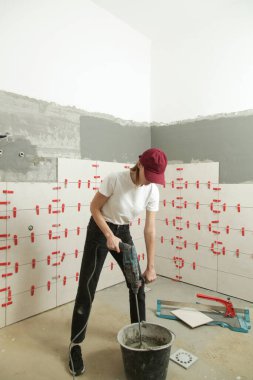 Kadın kovaya seramik fayans yapıştırıcısı karıştırıyor. Kovaya yapıştırıcıyı elle harç karıştırıcı ile karıştırıyorum. DIY ev geliştirme projesi.