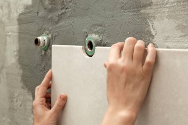 Banyo duvarlarını döşeyen bir kadın fayansa yapıştırıcı sürüyor ve seramik fayansları doğru pozisyona yerleştiriyor. Banyoya fayans döşeme işlemi adım adım yapılıyor. DIY Ev Geliştirme.