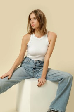 Klasik kıyafetli bir kadının stüdyo fotoğrafları. Mavi kot pantolon ve beyaz atlet.