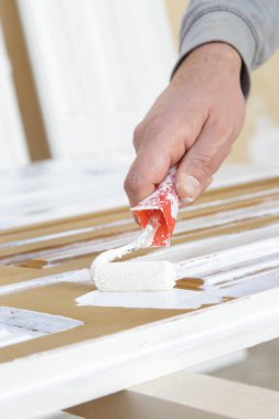 Boya silindiri. Beyaz ahşap bir kapının üzerini beyaz boyayla boyama işlemi.