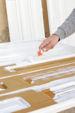 Boya silindiri. Beyaz ahşap bir kapının üzerini beyaz boyayla boyama işlemi.