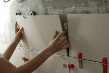 Banyo duvarlarını döşeyen bir kadın fayansa yapıştırıcı sürüyor ve seramik fayansları doğru pozisyona yerleştiriyor. Banyoya fayans döşeme işlemi adım adım yapılıyor. DIY Ev Geliştirme.