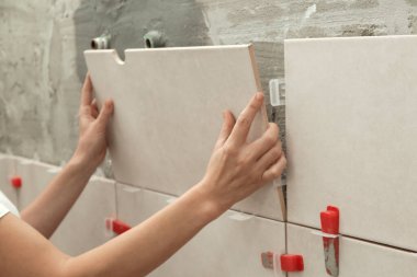 Banyo duvarlarını döşeyen bir kadın fayansa yapıştırıcı sürüyor ve seramik fayansları doğru pozisyona yerleştiriyor. Banyoya fayans döşeme işlemi adım adım yapılıyor. DIY Ev Geliştirme.