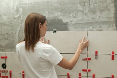 Banyo duvarlarını döşeyen bir kadın fayansa yapıştırıcı sürüyor ve seramik fayansları doğru pozisyona yerleştiriyor. Banyoya fayans döşeme işlemi adım adım yapılıyor. DIY Ev Geliştirme.
