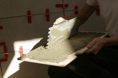 Banyo duvarlarını döşeyen bir kadın fayansa yapıştırıcı sürüyor ve seramik fayansları doğru pozisyona yerleştiriyor. Banyoya fayans döşeme işlemi adım adım yapılıyor. DIY Ev Geliştirme.