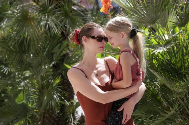 Sokakta sarılan bir anne ve kızın samimi portresi. Güzel bir yeşillik, yaz yaşam tarzı, aynı kahverengi kıyafetler, sevgi ve bağlılık duyguları.