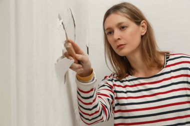 Duvardaki güherçile ya da küf sorunu. Kadın, sağlam bir yüzeye ulaşana kadar kötü durumdaki boya ve alçıyı kazıyıp çıkarmak için kazıyıcı kullanıyor..