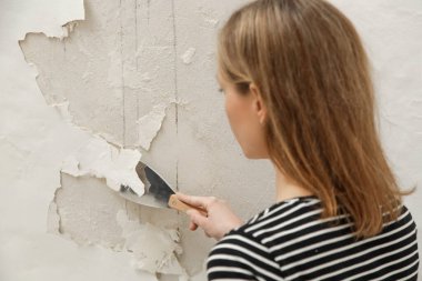 Duvardaki güherçile ya da küf sorunu. Kadın, sağlam bir yüzeye ulaşana kadar kötü durumdaki boya ve alçıyı kazıyıp çıkarmak için kazıyıcı kullanıyor..