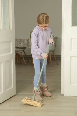 Çocuk süpürgeyle yerleri süpürüyor. Bir çocuğun rutinindeki angarya işleri de dahil olmak üzere daha fazla özsaygı, daha fazla sorumluluk ve hüsranla daha iyi başa çıkabilirsiniz.