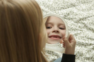 7 yaşında tatlı bir kız aynaya bakıyor ve ön dişleri çıkıyor. 