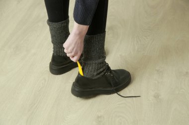 Woman is putting on shoes using yellow plastic shoehorn. clipart