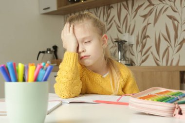 Yorgun ilkokul kızı, zor bir görevle, mutfak masasında oturarak ev ödevi yapmaktan yoruldu. Evde eğitim, evde eğitim kavramı.