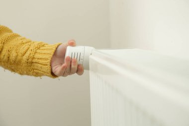 Çocuğun eli radyatör termostat vanasını ayarlıyor, merkezi ısıtma sistemini kontrol ediyor
