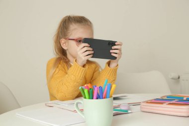 Küçük kız mutfak masasında ödev yaparken cep telefonu kullanıyor.