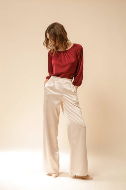 Stüdyo fotoğrafları, sade ipek saten elbiseler, bordo bluz ve bej geniş paça pantolon giyen genç kadın modeller..
