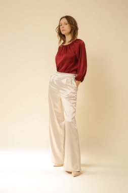 Stüdyo fotoğrafları, sade ipek saten elbiseler, bordo bluz ve bej geniş paça pantolon giyen genç kadın modeller..