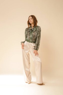 Stüdyo fotoğrafları, güzel sonbahar kıyafetleri giyen genç kadın modeller, sonbahar desenli yeşil boho bluz ve bej saten geniş paça pantolon.