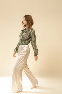 Stüdyo fotoğrafları, güzel sonbahar kıyafetleri giyen genç kadın modeller, sonbahar desenli yeşil boho bluz ve bej saten geniş paça pantolon.