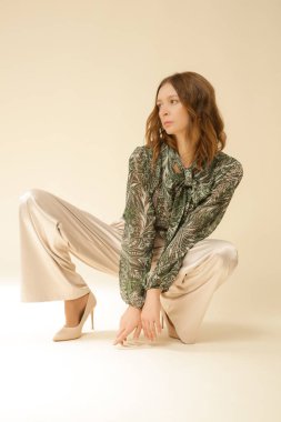 Stüdyo fotoğrafları, güzel sonbahar kıyafetleri giyen genç kadın modeller, sonbahar desenli yeşil boho bluz ve bej saten geniş paça pantolon.