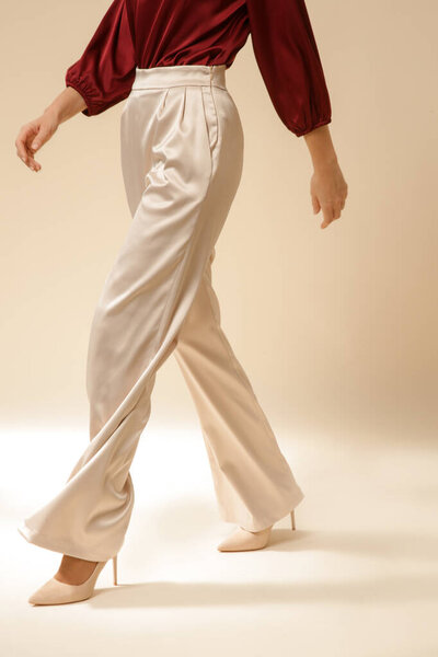Serie of studio photos of young female model wearing simple silk satin  beautiful outfit, burgundy blouse and beige wide leg trousers.