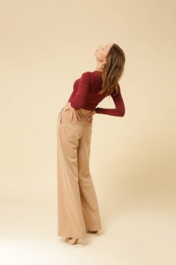 Stüdyo fotoğrafları, basit güzel kıyafetler, kırmızı v yaka gömlek ve bej geniş paça pantolon giyen genç kadın modeller.