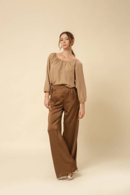 Stüdyo fotoğrafları, bej ipek saten elbise, bluz ve geniş paça pantolon giyen kadın modeller..