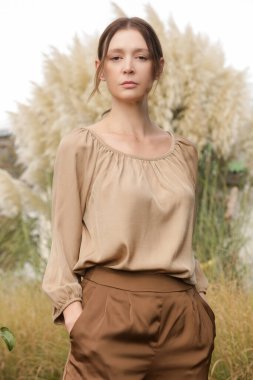 Açık havada bej rengi ipek saten elbise, bluz ve geniş paça pantolon giyen genç bir kadının portresi. Sonbahar moda koleksiyonu.